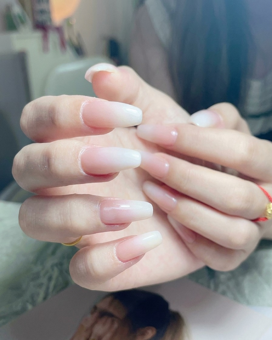 A brush applying a final layer of clear, glossy top coat to a finished white ombre nail.