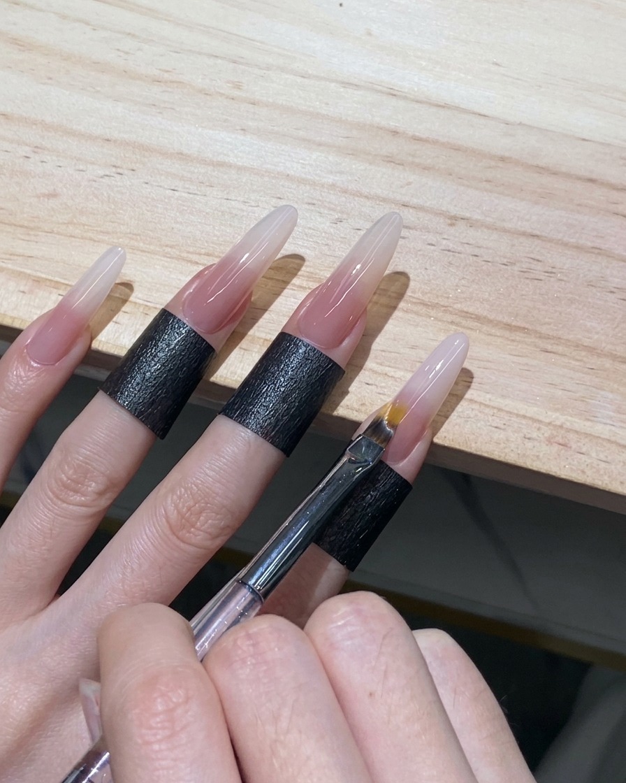 An ombre brush using light sweeping motions to diffuse the edge of white gel on a stiletto nail.