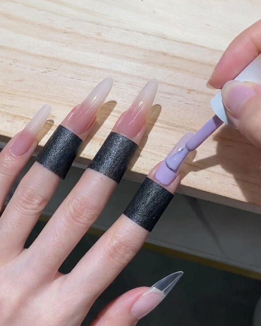 A gel polish brush filling the lower half of a stiletto nail with sheer nude gel, bringing it up to meet the diffused white edge.