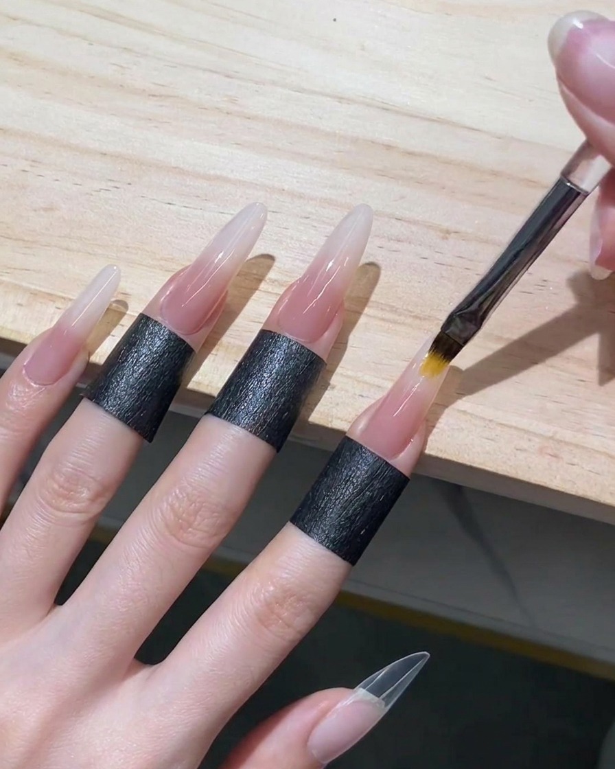 An ombre brush blending sheer nude gel upwards into wet white gel on a stiletto nail to create a seamless gradient.