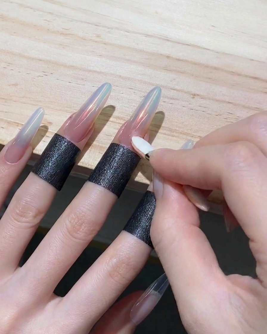 A hand using a small sponge applicator to rub iridescent orange powder onto the tip of a long nail.
