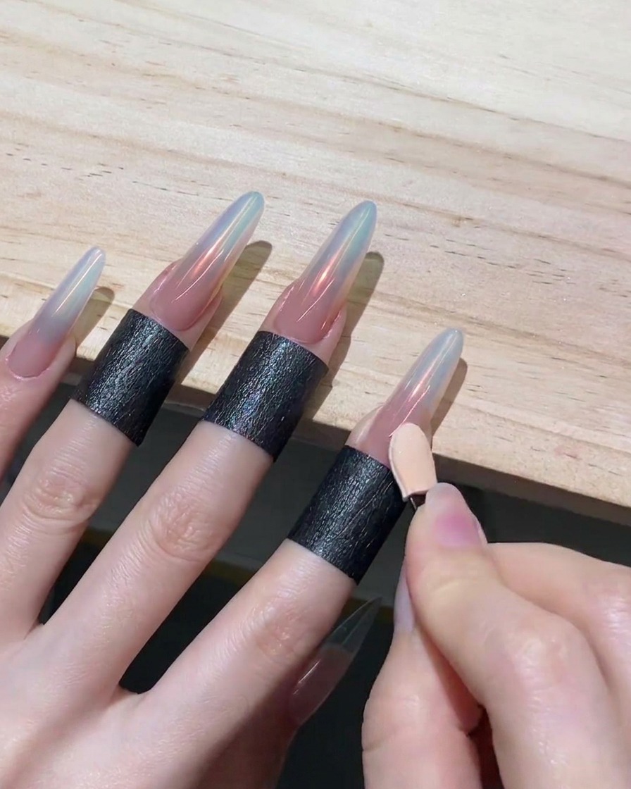 A hand using the clean side of an eyeshadow sponge applicator to drag chrome powder downwards on a nail, creating an ombre effect.