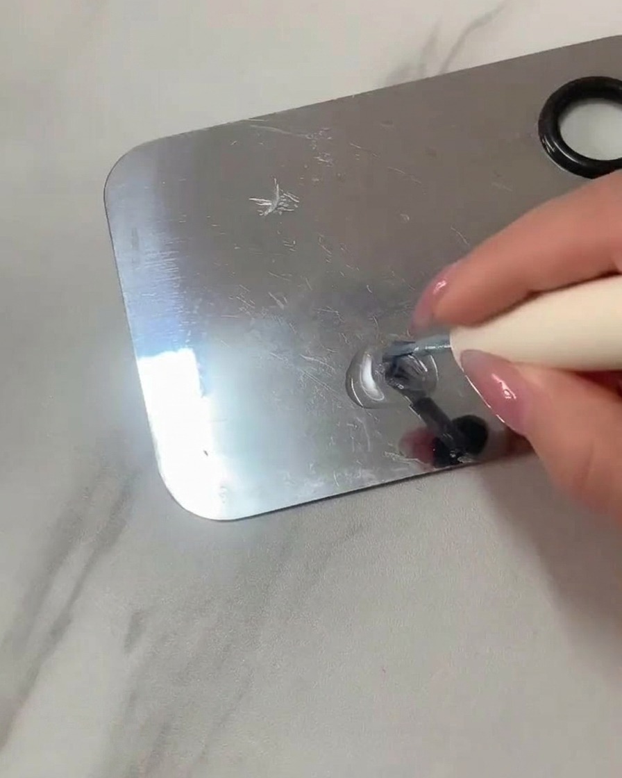A flat gel brush mixing clear gel and light blue polish on a stainless steel makeup palette.