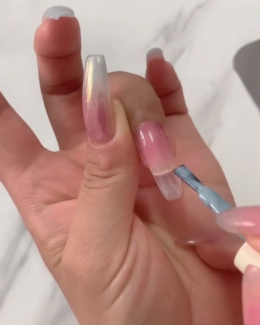 A close-up of a gel brush applying light blue gel polish to the top half of a clear long coffin nail tip.