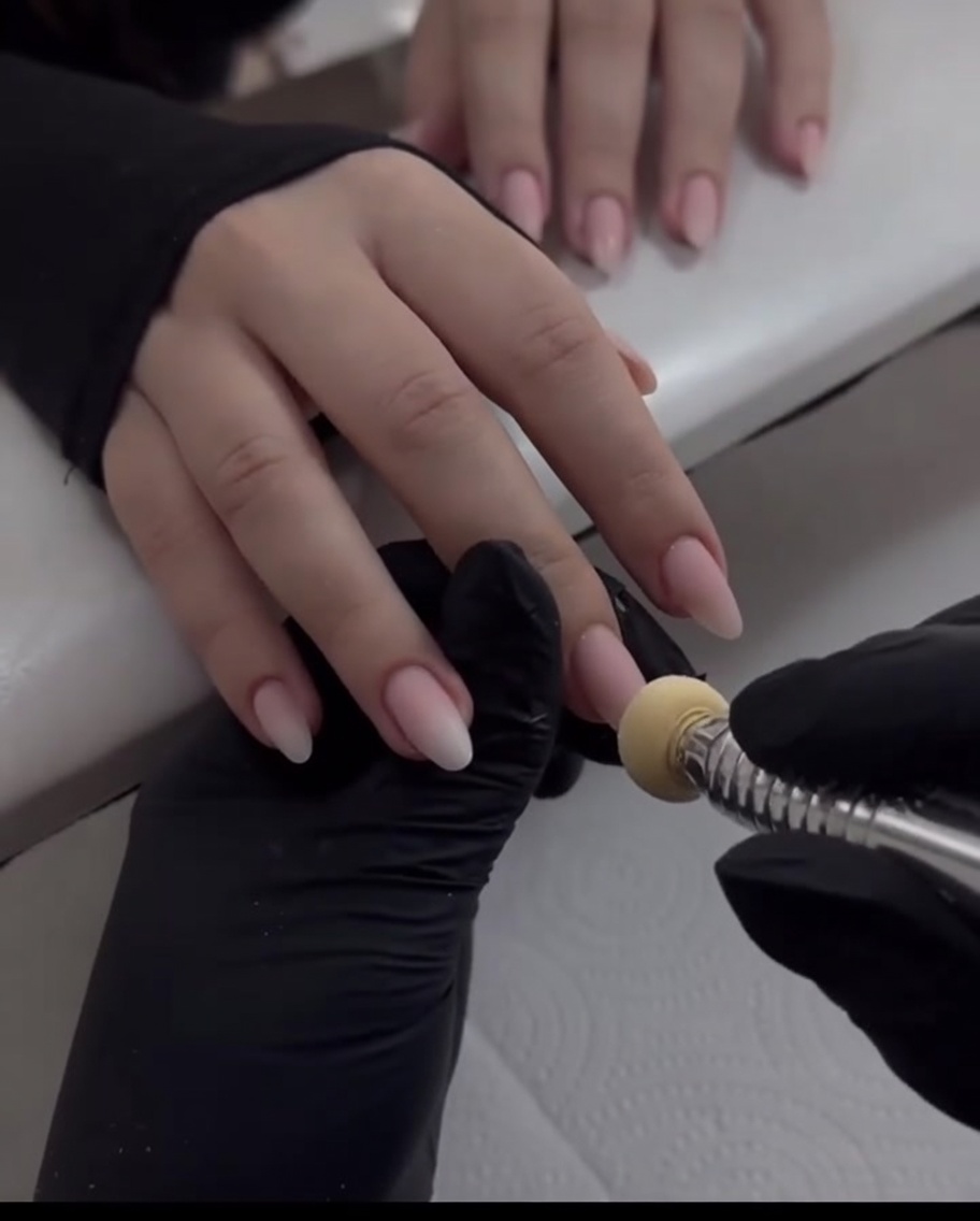 A close-up shot of a sponge applicator dabbing pearlescent chrome powder onto the tip of a middle fingernail.