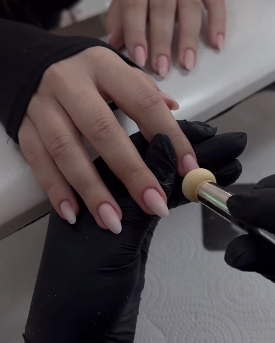 Buffing pearl chrome powder onto an almond-shaped fingernail until it creates a shiny, reflective mirror finish.