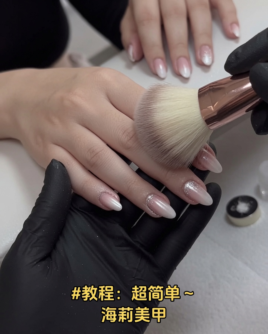 A large, fluffy pink makeup brush sweeping over manicured fingernails to remove excess chrome dust.