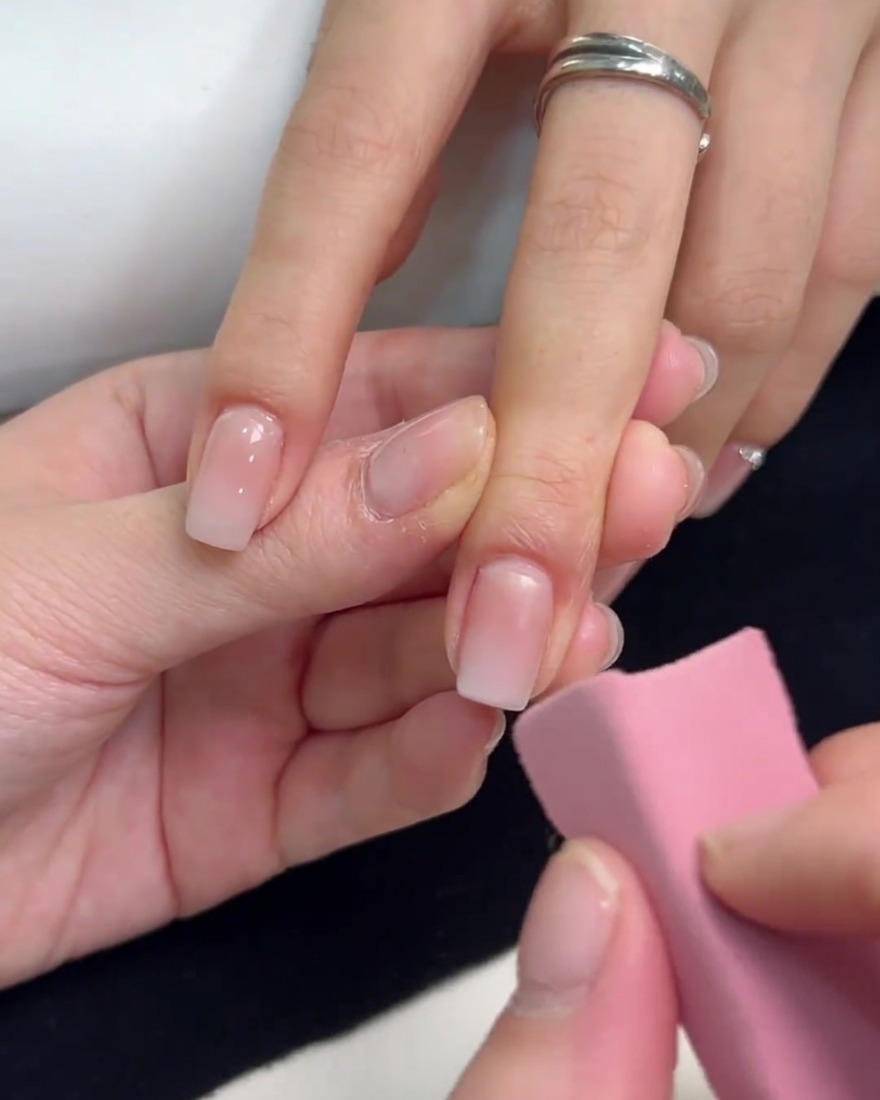 A pink sponge being used to dab white gel polish onto the tip of a square nail, blending it down to create an ombre effect.