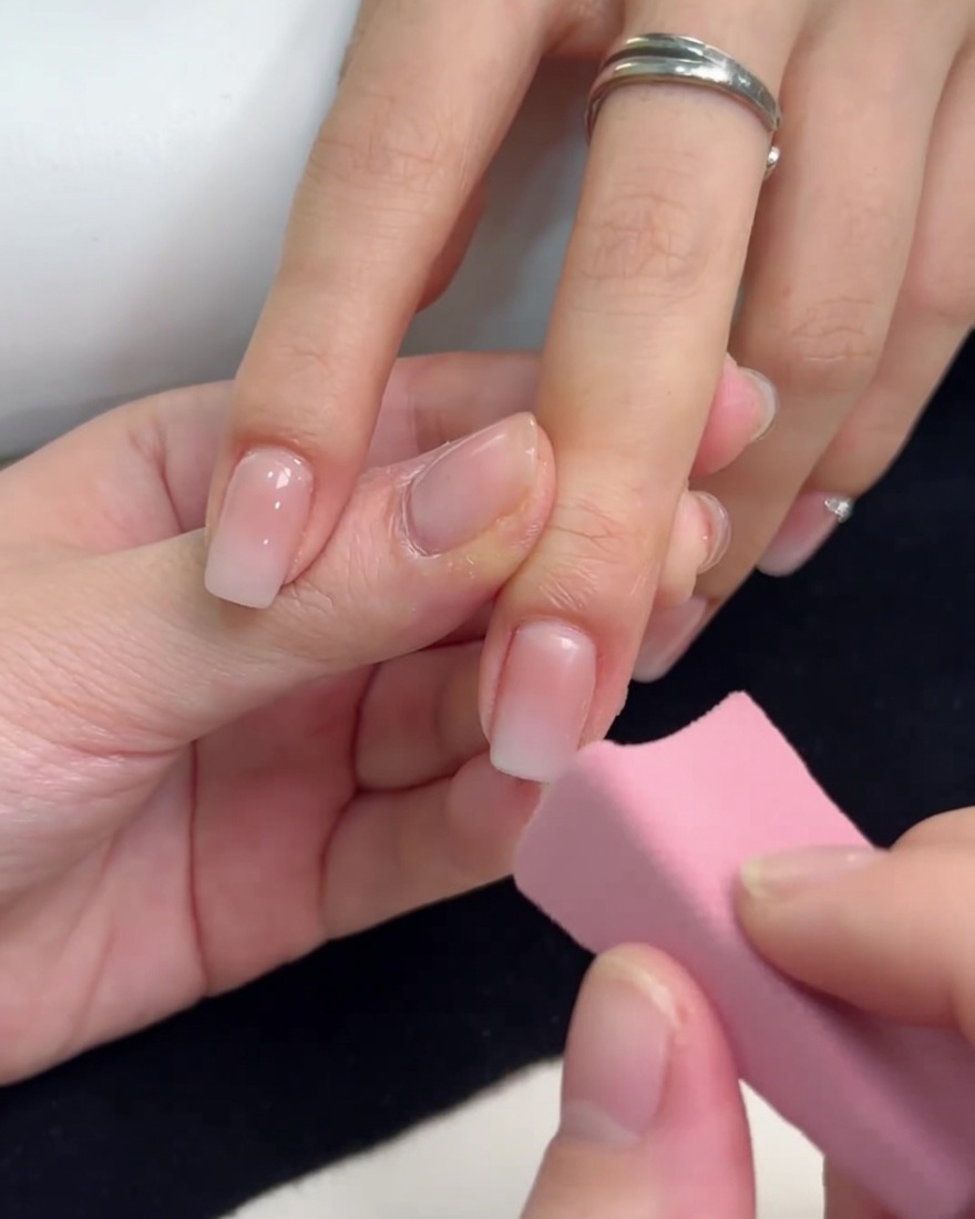 A small pink sponge dabbing white gel onto the tip of a fingernail to create an ombre effect.