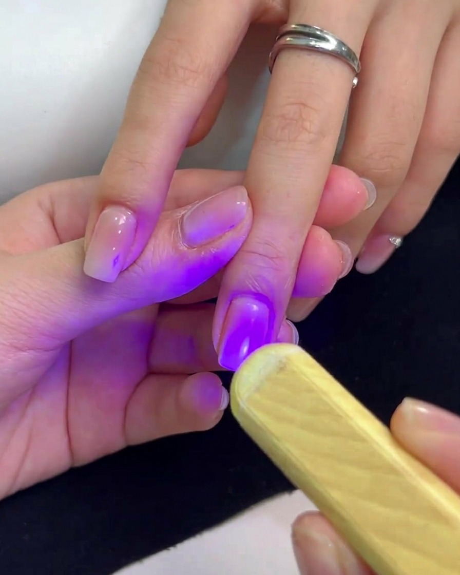 A mini handheld UV lamp emitting purple light held over a fingernail to cure the gel polish.