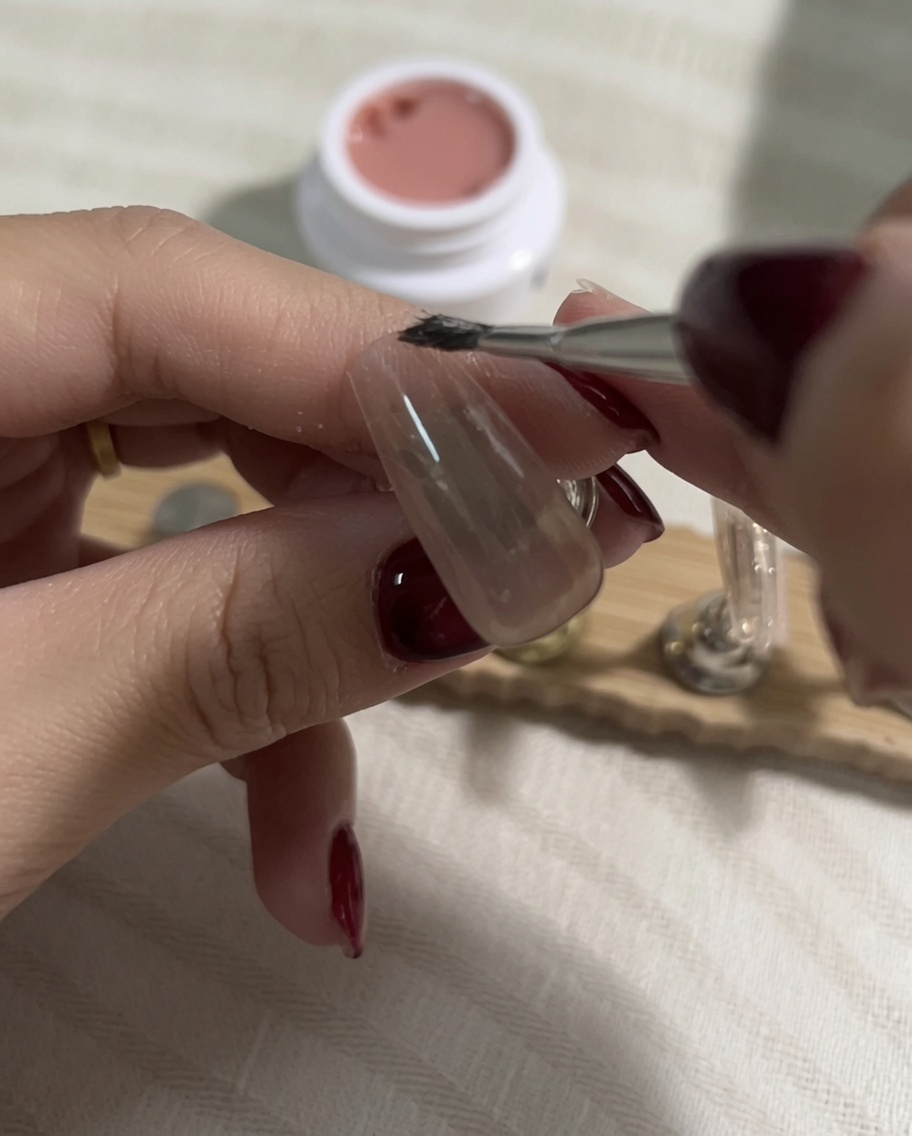 Picking up a lighter shade of nude gel polish on a flat brush after the previous layer has been cured.
