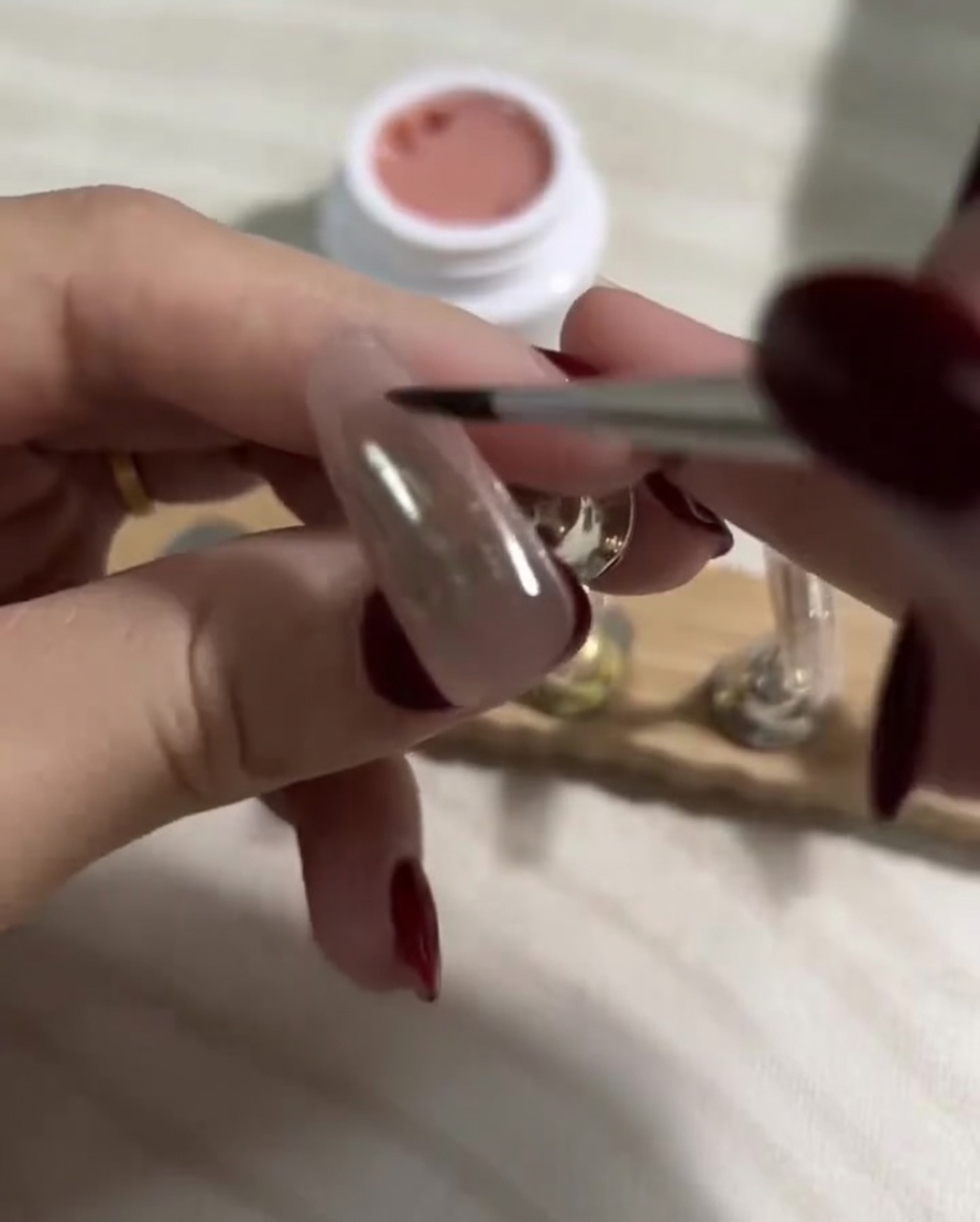 Brushing a smooth layer of light nude gel polish over the already cured darker base layer on a press-on nail.