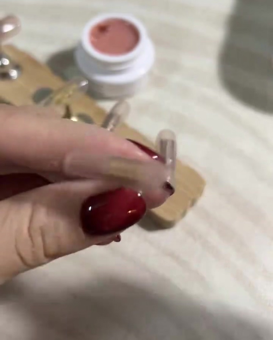 A close-up shot of a hand using a lint-free wipe soaked in gel cleanser to clean the surface of cured press-on nails.