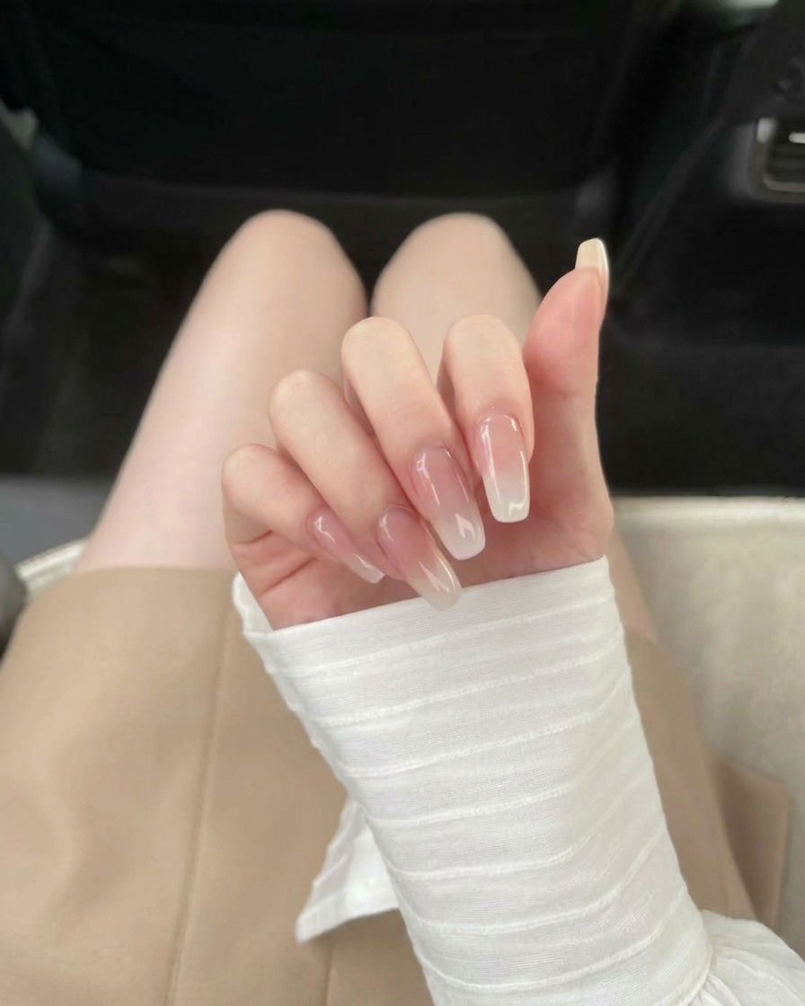 A brush applying a clear base coat onto a transparent nail extension.