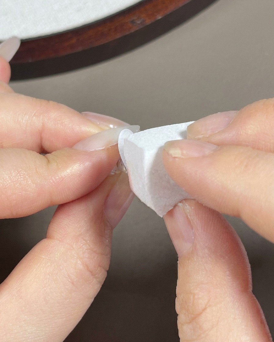 A makeup sponge dabbing white gel onto the tip of a long almond nail.