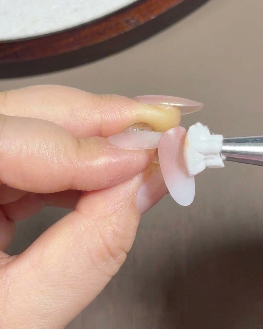 A sponge brush blending pink gel onto the mid-section and cuticle area of the nail.