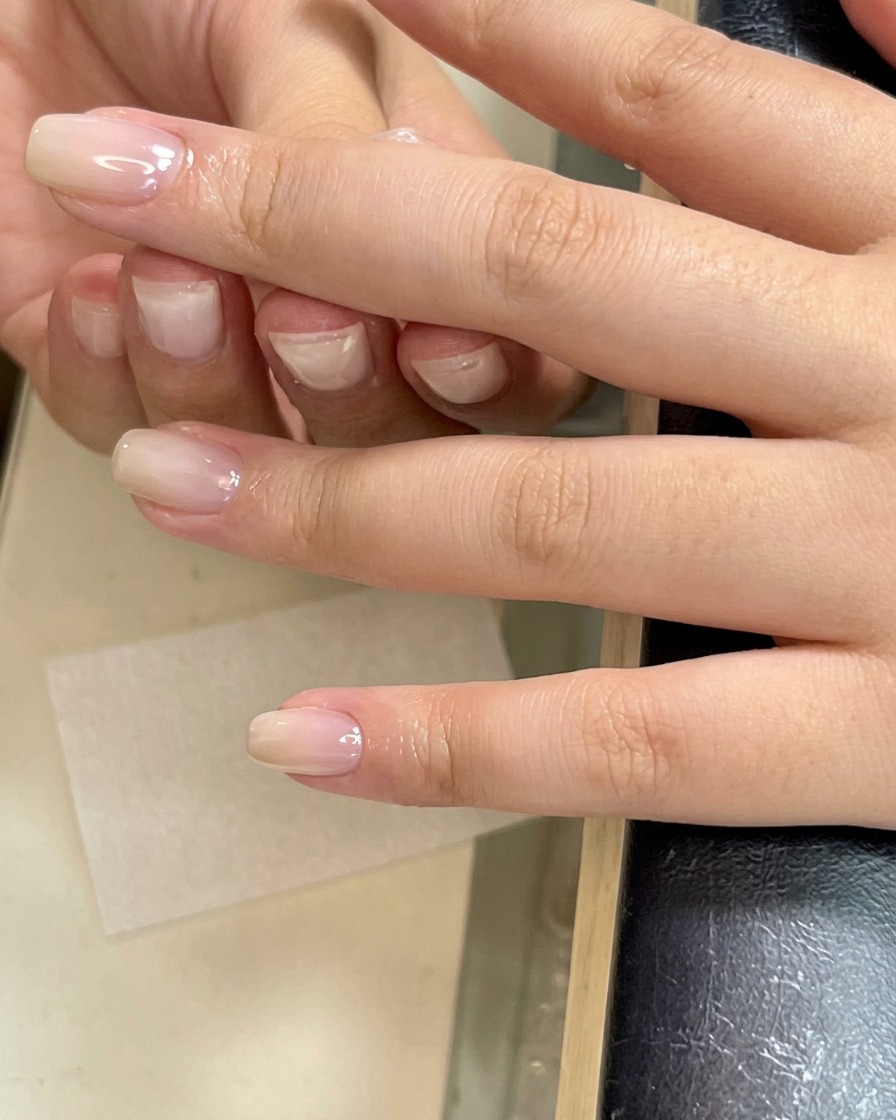 A hand using a lint-free wipe to clean the surface of a nail that has just finished curing under a lamp.