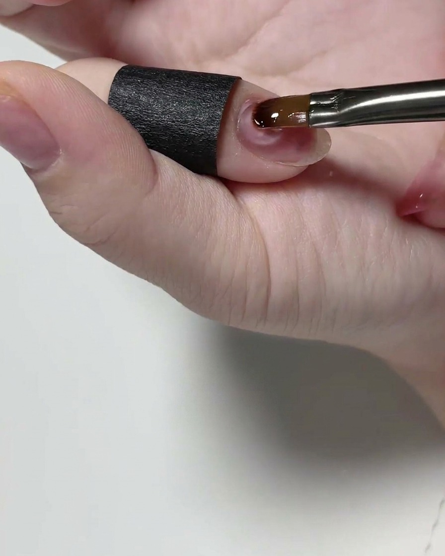 A detail brush applying a clear structural gel to a natural fingernail.