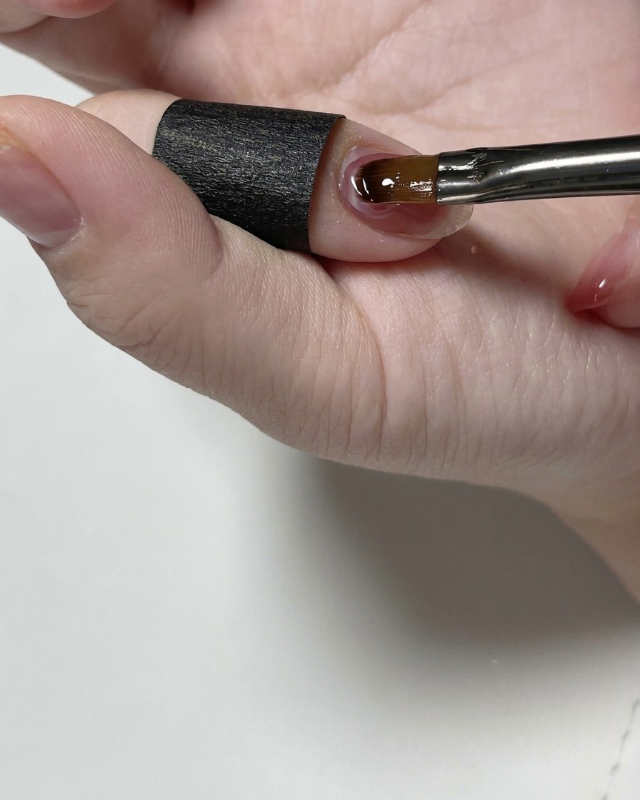 A fine detail brush smoothing clear structure gel near the cuticle of a fingernail.
