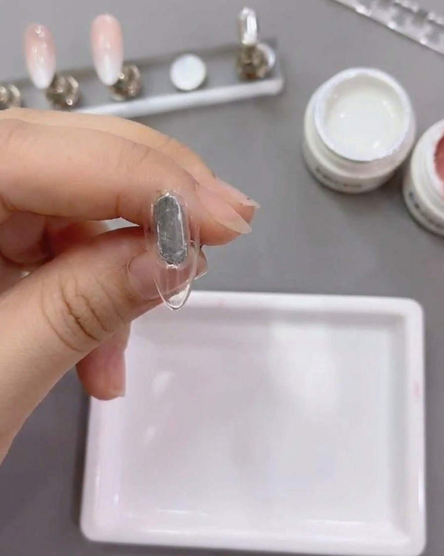 A flat brush applying white gel number 79 onto a natural nail tip.