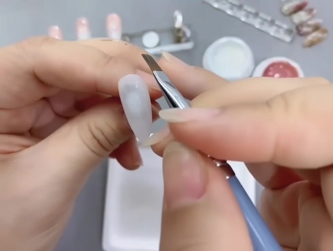 An angled nail art brush applying nude gel polish onto the lower half of a white-painted nail tip.