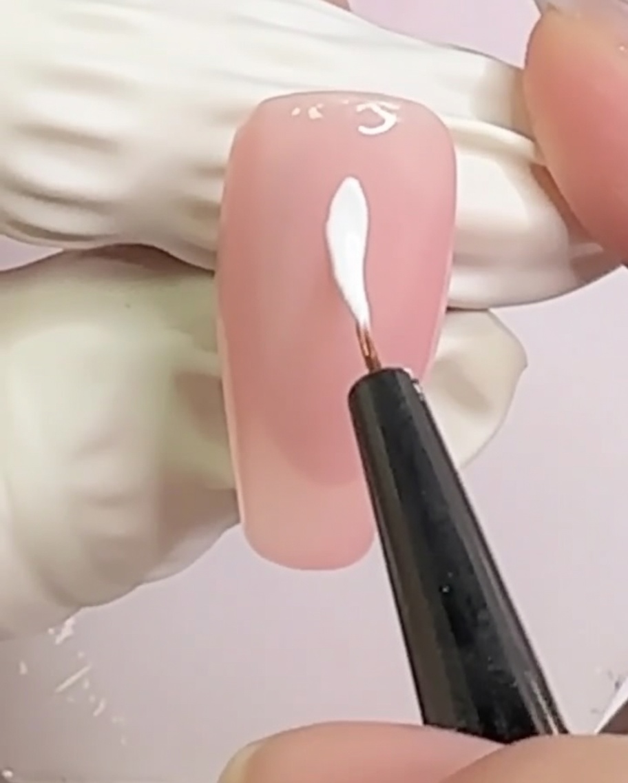 A nude nail with two white crossing lines forming an X pattern in the center.
