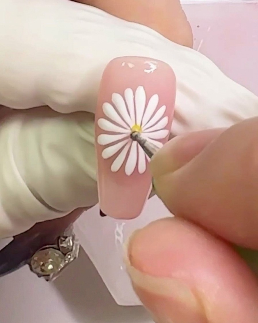 A close-up shot showing a yellow gel dot being applied to the center of the white daisy design.