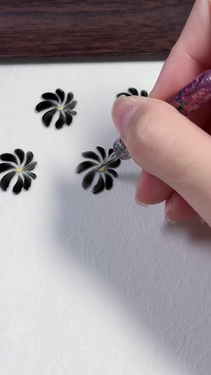 Three hand-painted black daisy flowers with yellow centers on a clean white surface.
