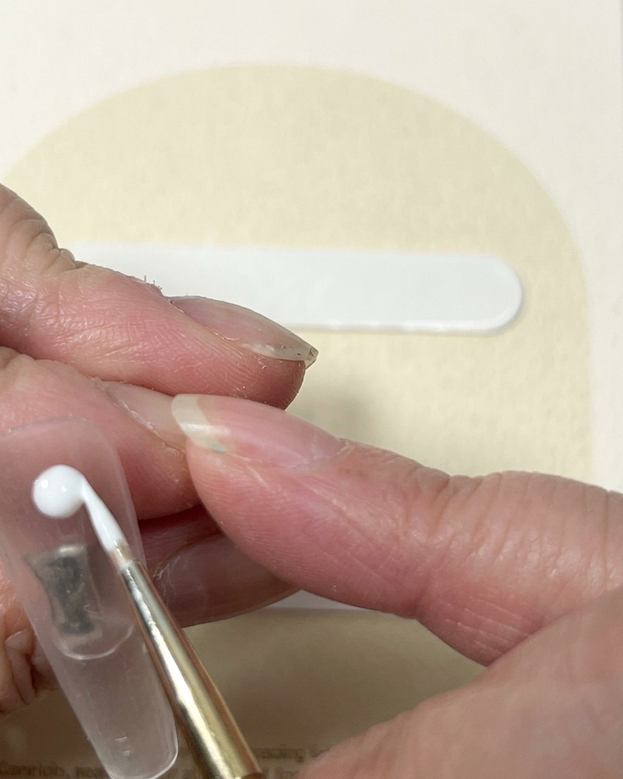 A liner brush pulling white gel from a central point to create the swirling look of a rose bud.