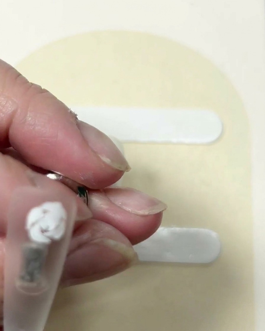 A close-up view of a partially formed white rose on a nail, with distinct curved strokes defining the outer layers.
