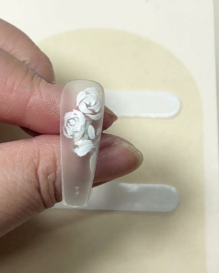 A tissue being pressed onto a freshly painted five-petaled white flower on a nail to soften the texture.