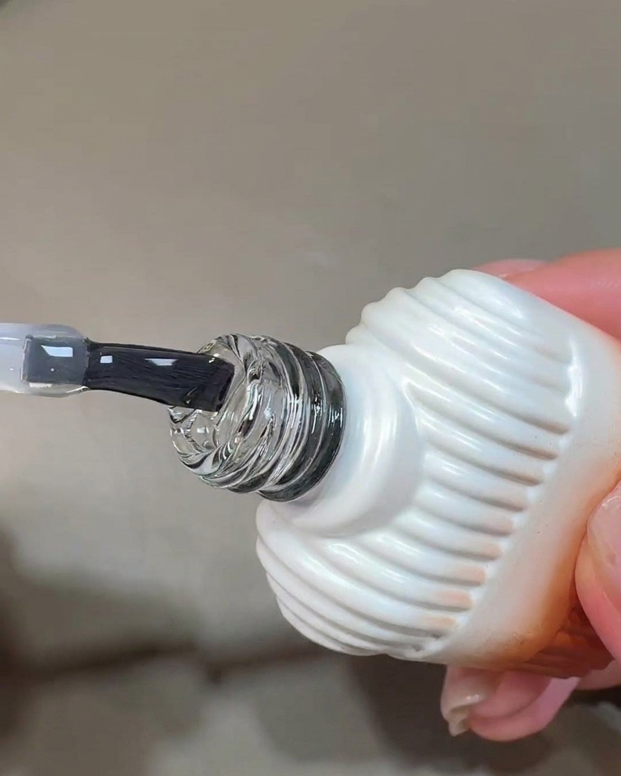A brush applying a clear, glossy layer of blooming gel onto a prepped nail surface.