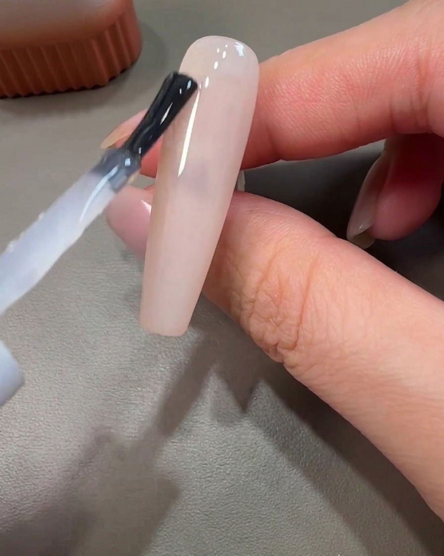 A close-up of a liner brush applying pink gel in a circular motion on an uncured base.