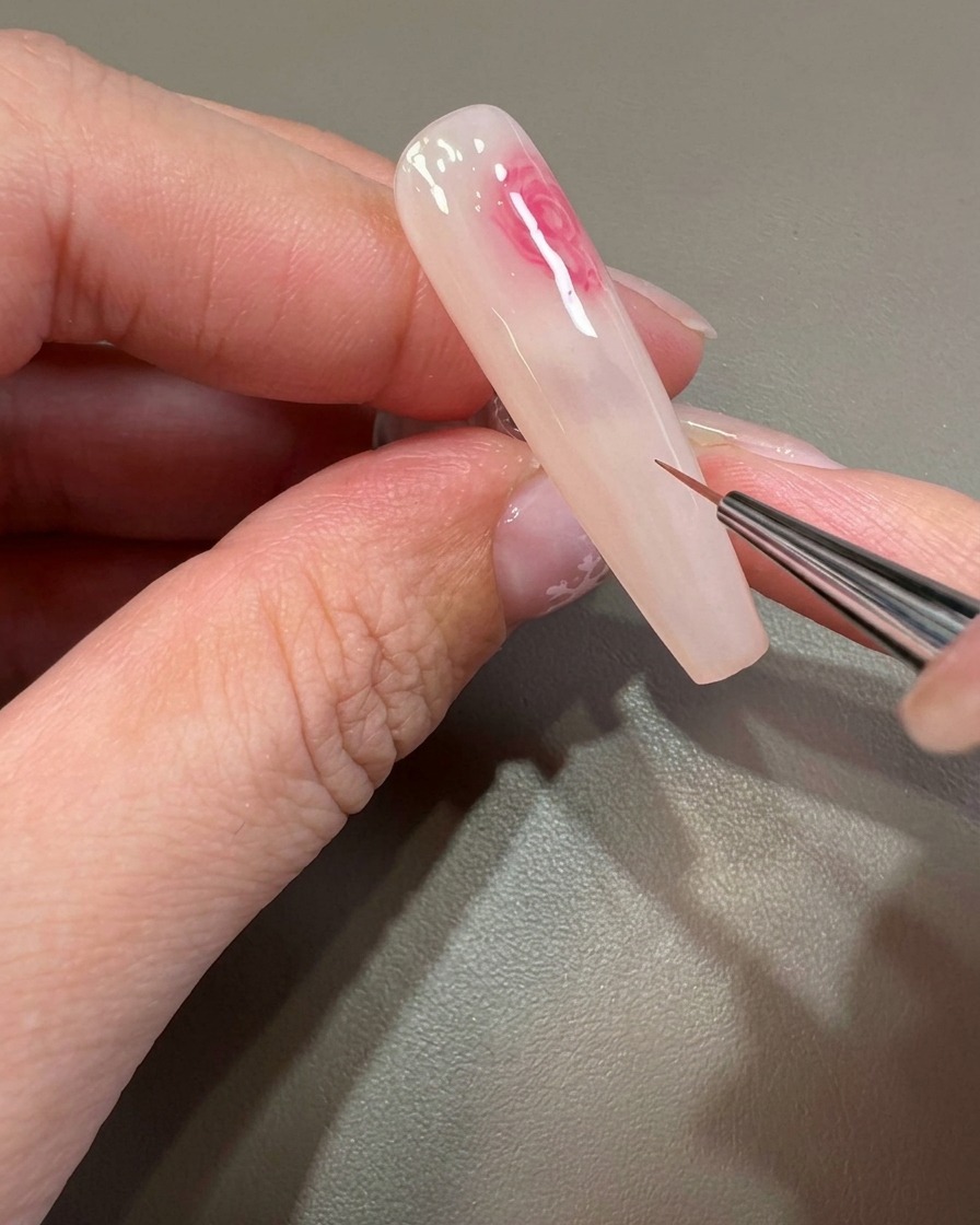 A fine brush detail-working on a pink, soft-focus bloom pattern on the nail.