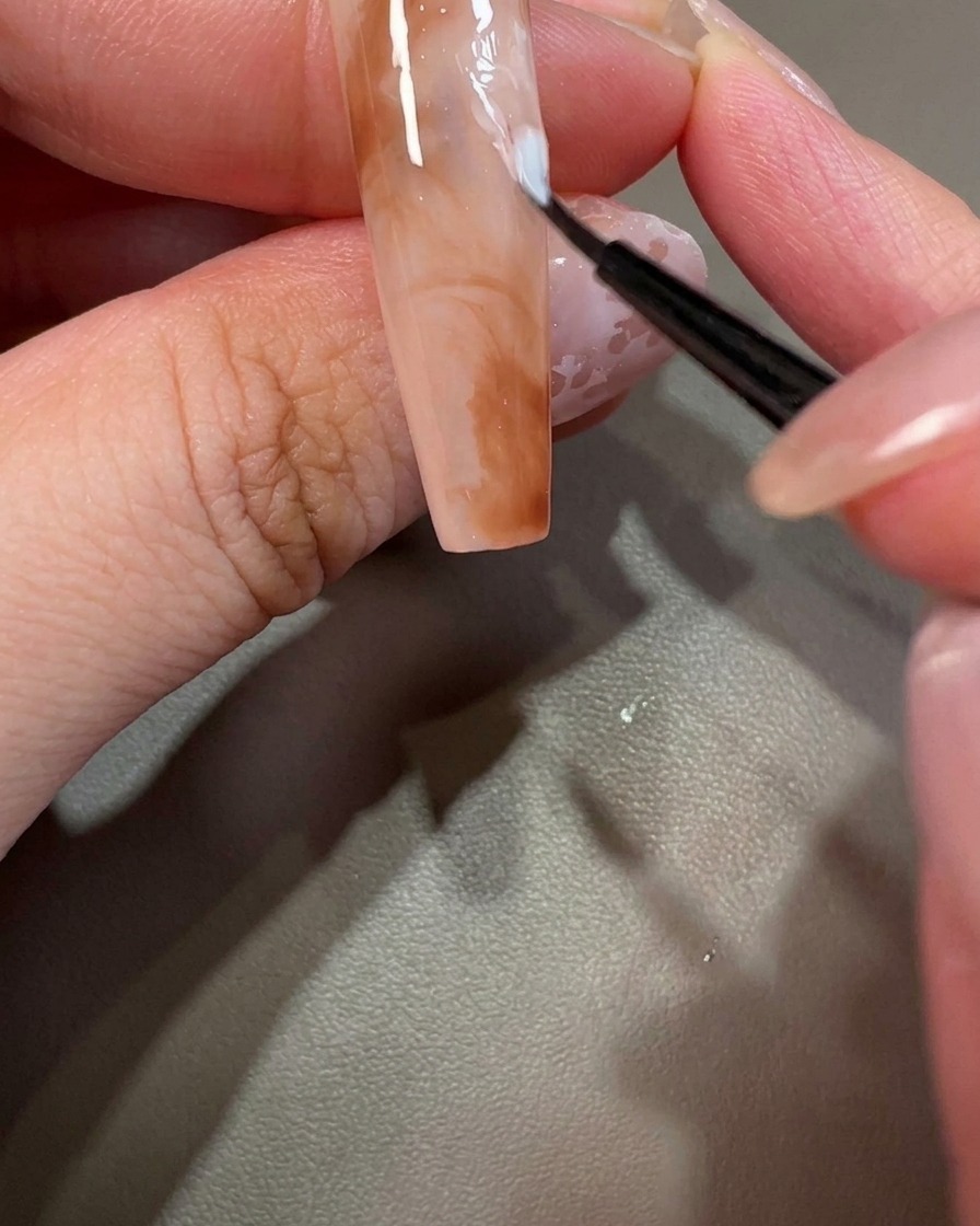 A close-up view of a nail being decorated with a tiny dot of white gel polish.