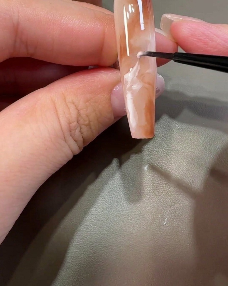 A liner brush pulling white gel through the brown design to create swirling marble patterns.