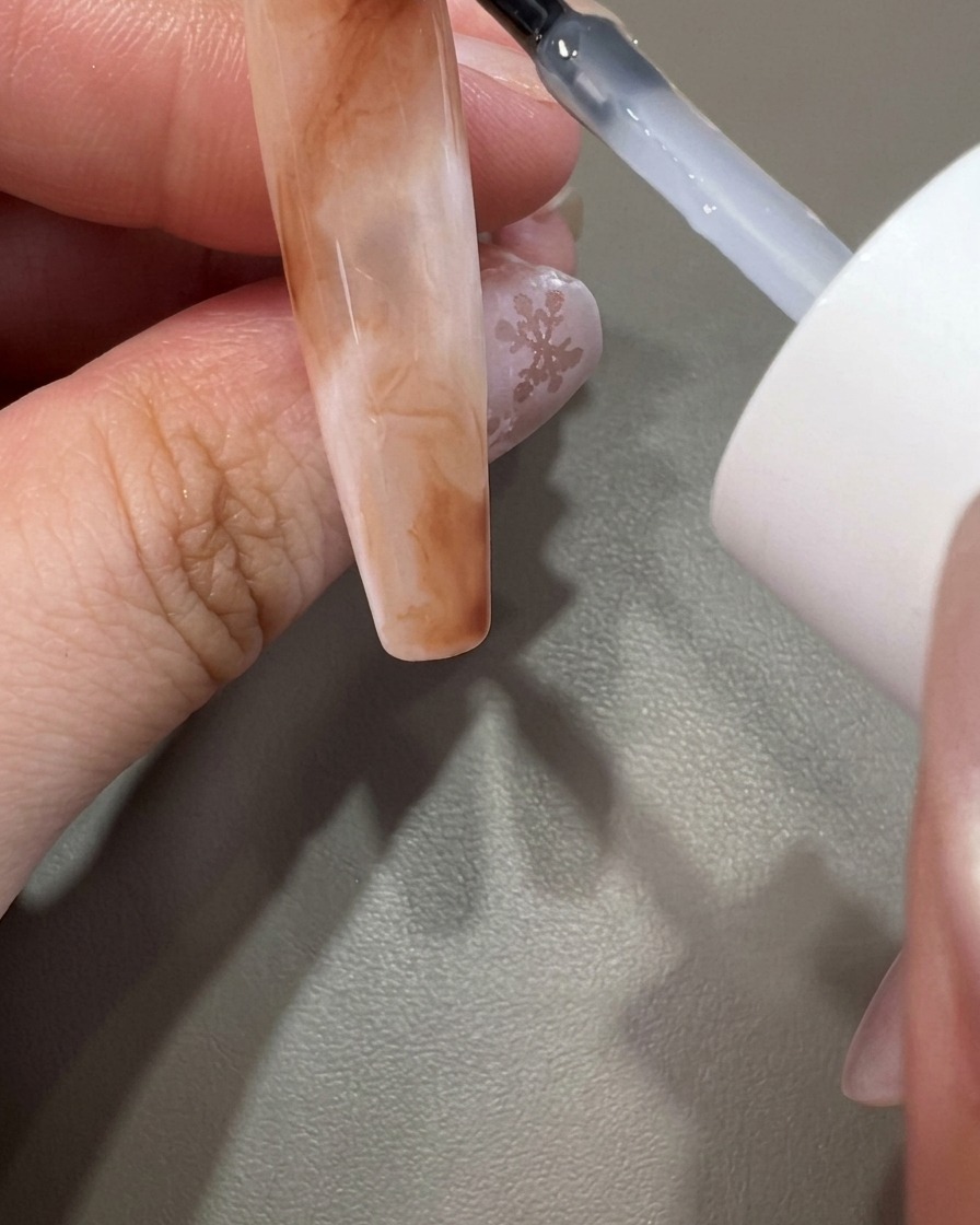 A brush applying clear top coat over a completed marble nail design.