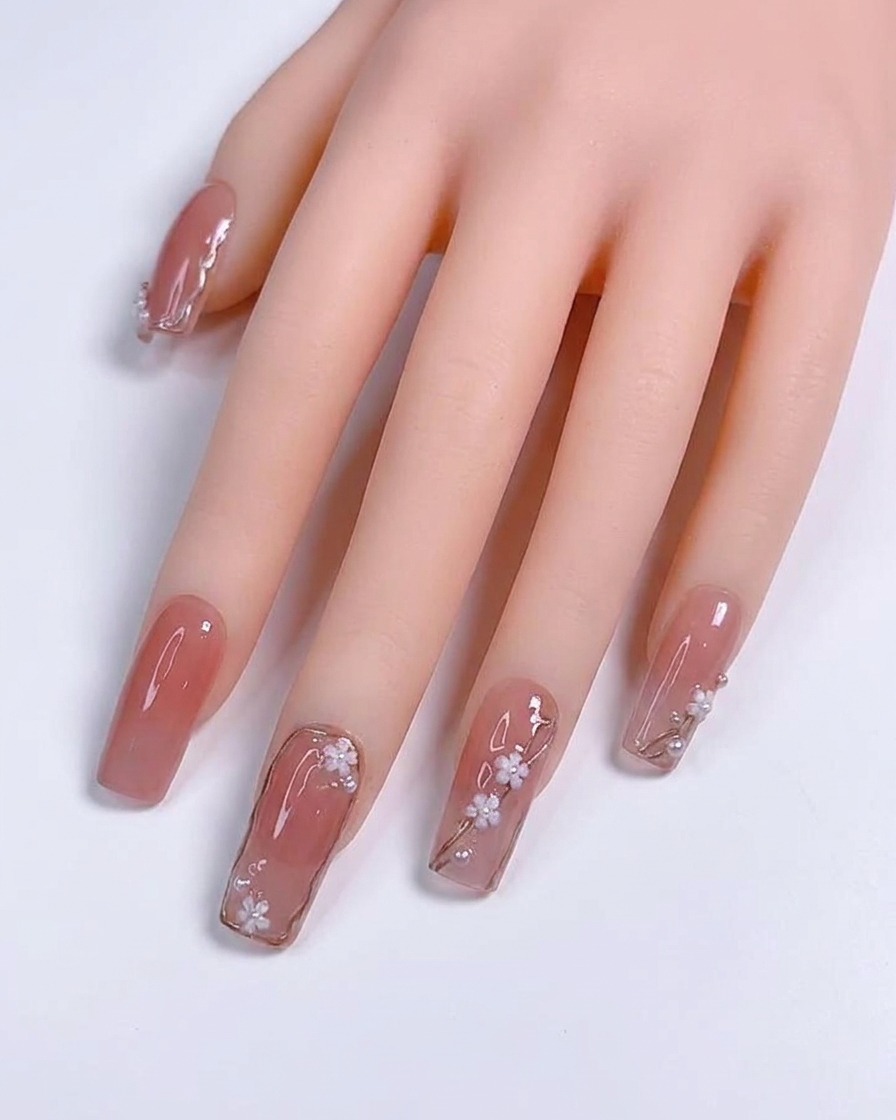A close-up of a detail brush applying thin metallic silver lines over a nude-colored gel nail.