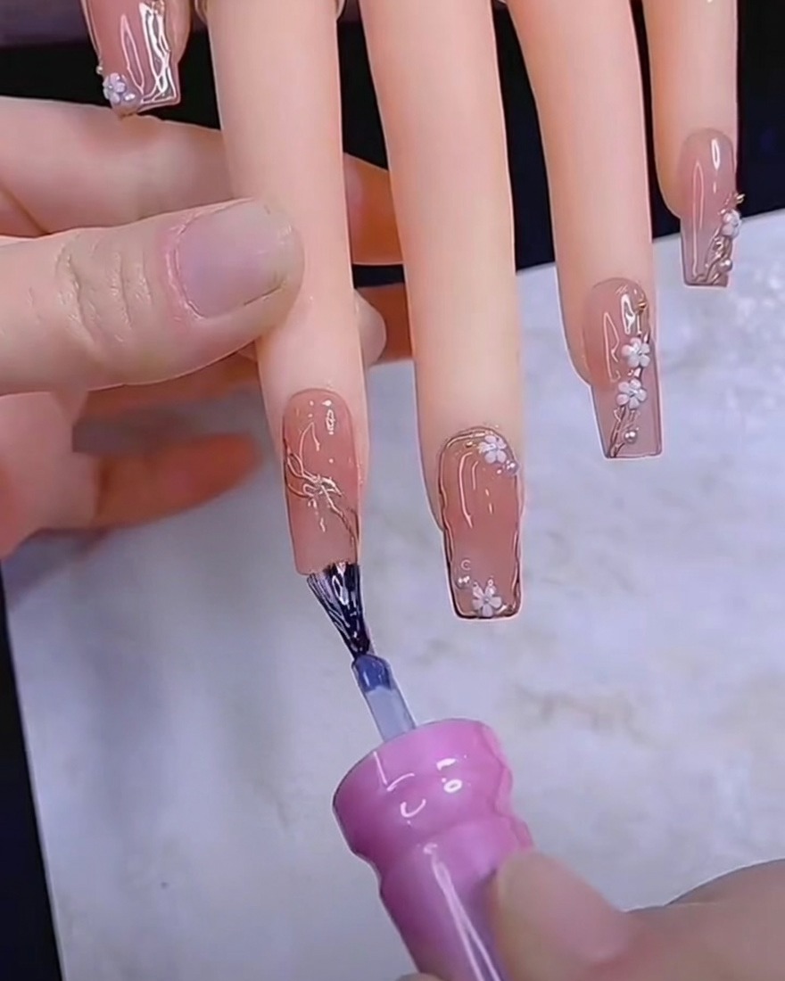 A dotting tool placing small white flower petals onto a gel nail.