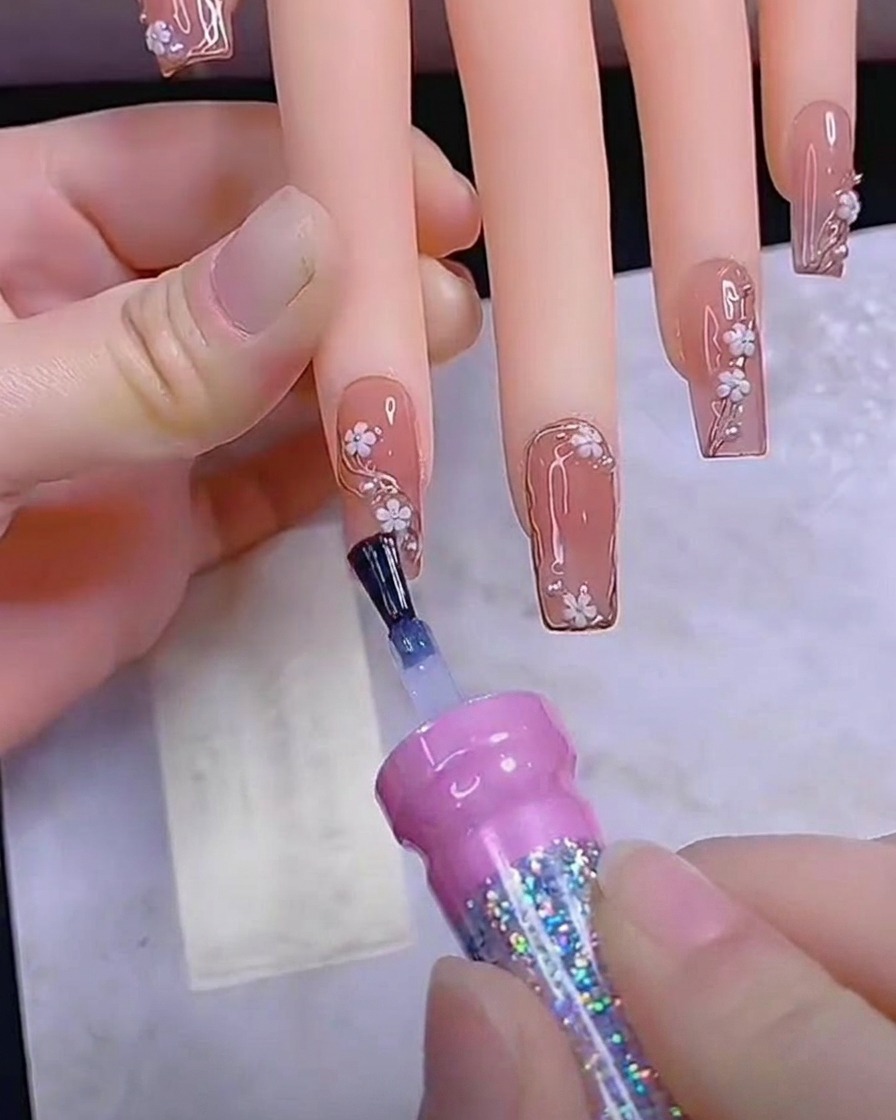 A brush applying a final, smooth layer of glossy top coat to a fully decorated nail.