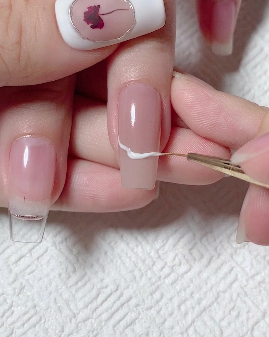 A fine liner brush drawing a wavy white line across the center of a nude-colored nail.