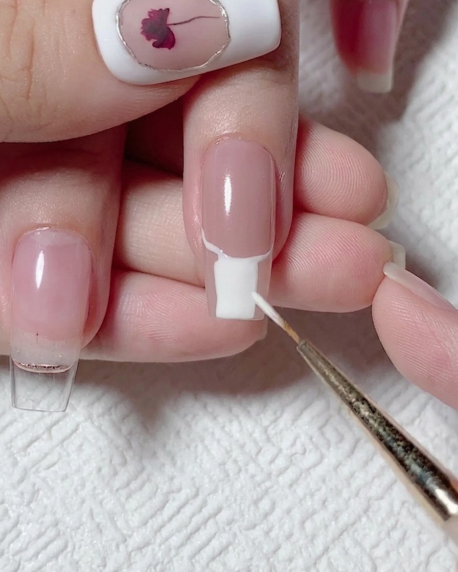 A flat brush filling the lower portion of a nail with opaque white gel polish.