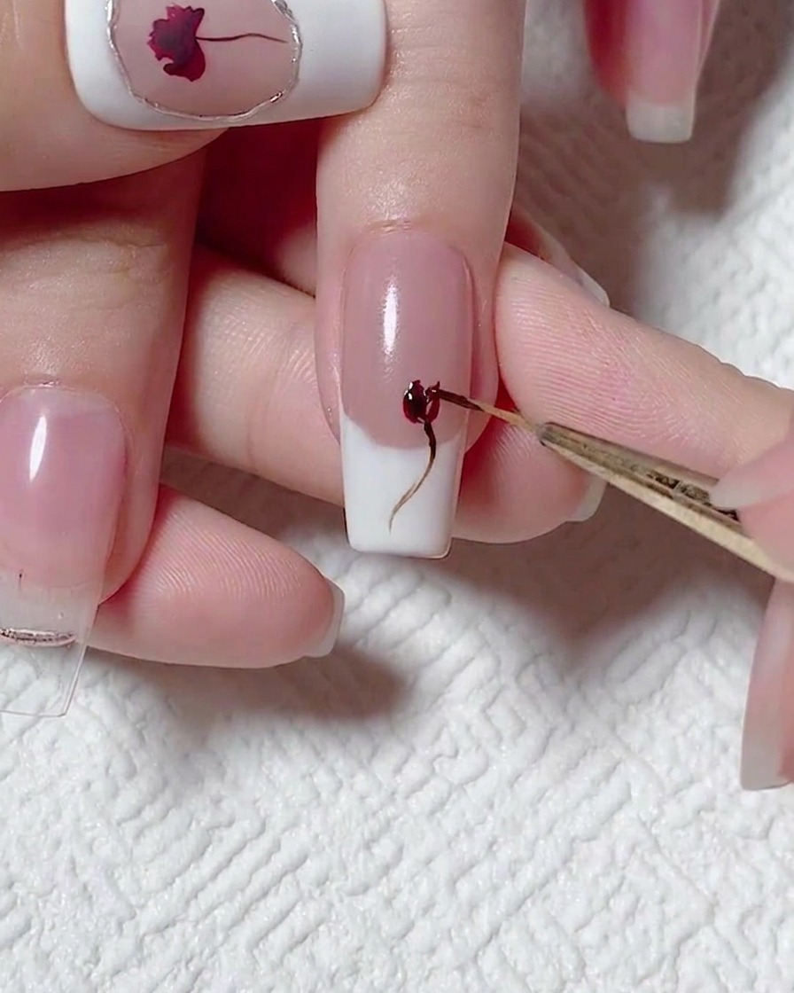 A close-up view of a detail brush adding depth to the rose design with red gel polish.