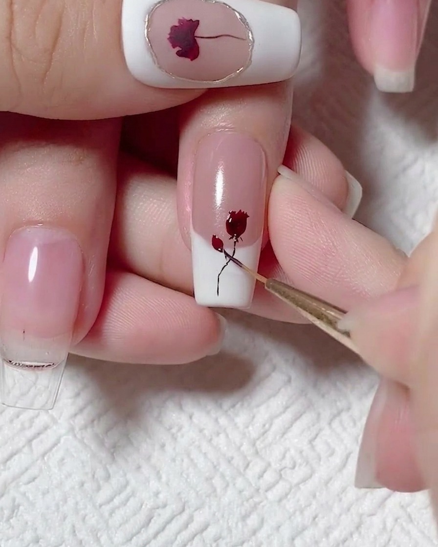 A fine liner brush adding tiny dark leaves to a painted black stem and red rose design on a nail.