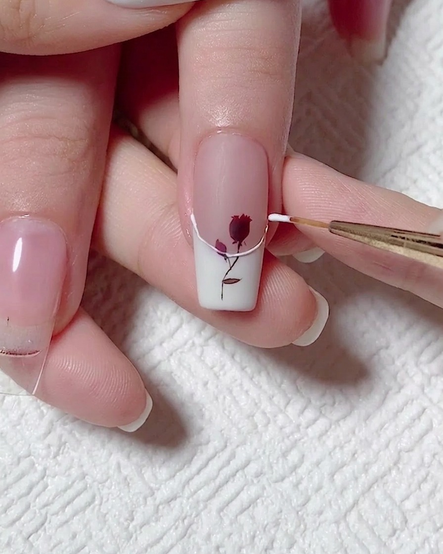 A thin liner brush carefully outlining the wavy smile line of a white French tip using clear 3D relief gel.
