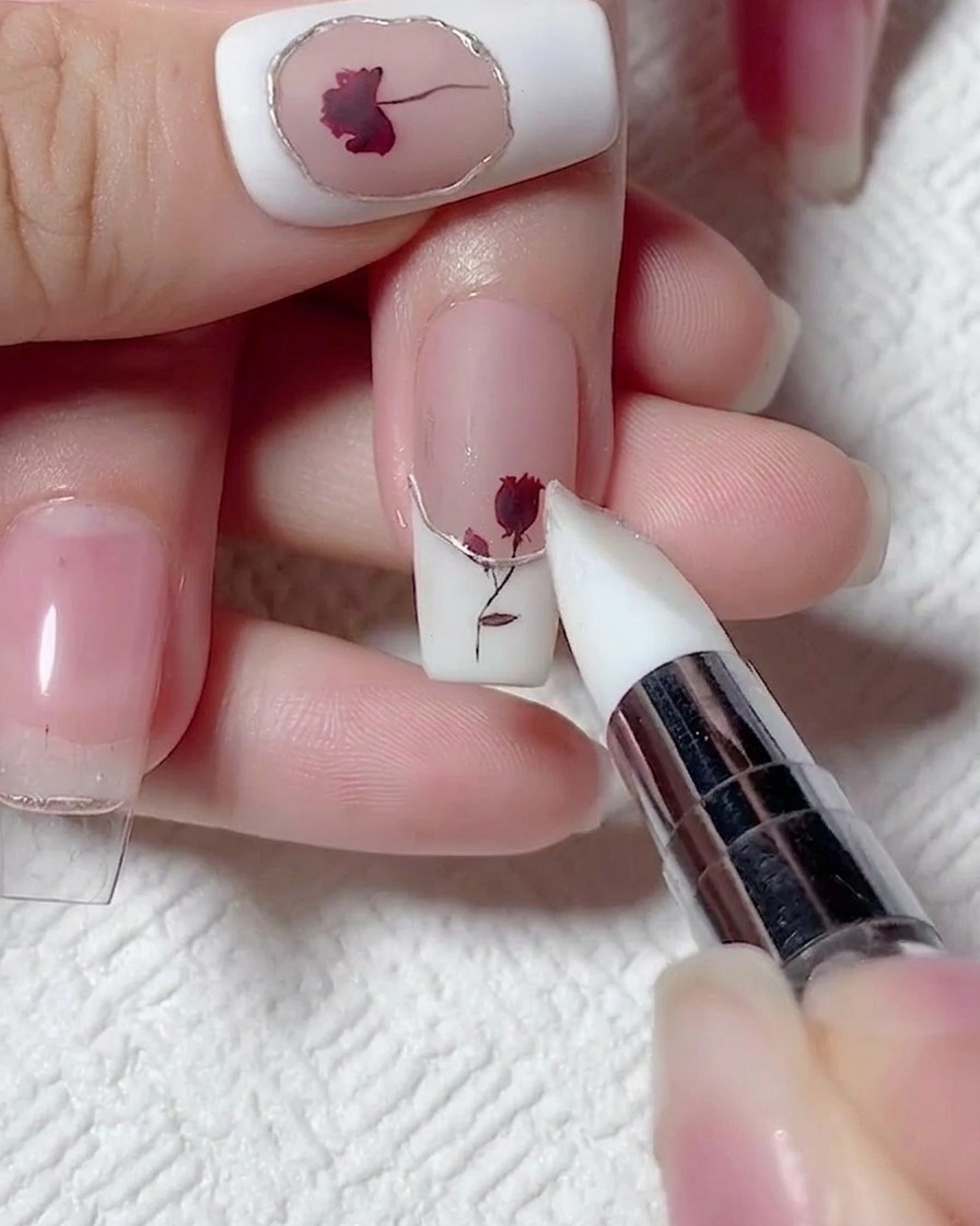 A pointed silicone tool rubbing champagne gold chrome powder onto a raised 3D border on a French manicure.