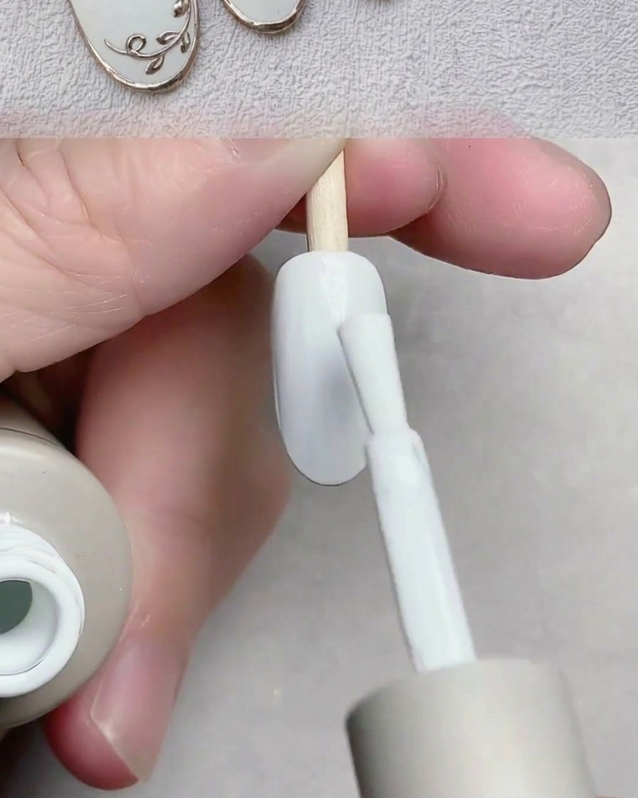 A brush applying smooth white gel polish over the nail plate of a nail tip.