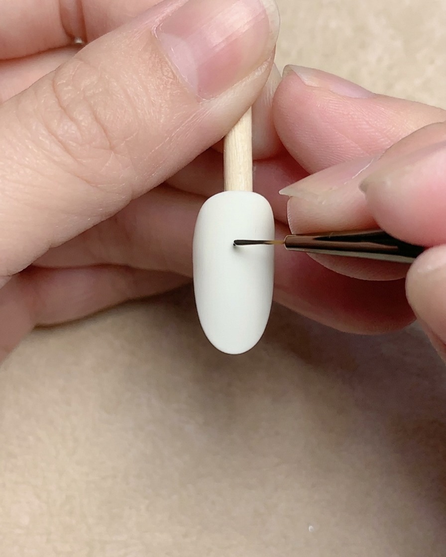 A close-up of a nail brush drawing a tiny black spiral on a white nail surface.