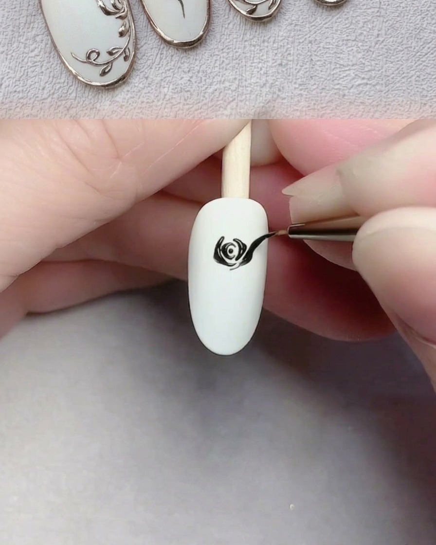 A nail art brush painting large, sweeping black petals onto a white nail to complete a rose.