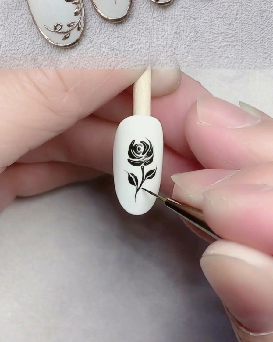 A close-up of a liner brush drawing a thin black line representing a stem on a white gel-coated nail.